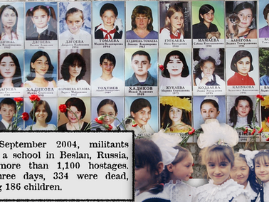 Photos of children and adults are displayed with red flowers below, commemorating the 2004 Beslan school siege victims. somber mood.