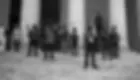 Men stand on stone steps, holding rifles, in front of a building with columns. The mood is tense and serious. The image is black and white.