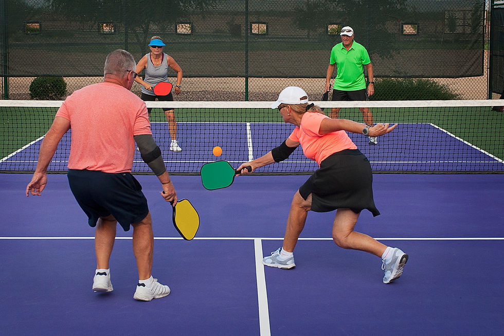 Two adult pickleball players reaching for a shot at the net during a doubles match on an outdoor court, demonstrating active movement and coordination.