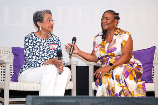 A woman reaches out holding a microphone and another woman smiles back