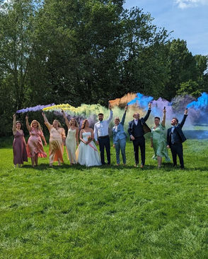 Bride and Groom and their friends hold colourful smoke bombs and walk in a line