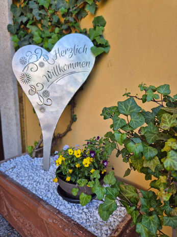 Metallherz mit Aufschrift „Herzlich Willkommen“ im Blumenkasten