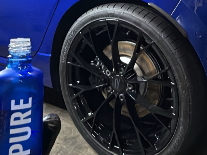 Gloss black wheel on a blue car next to a Gyeon coating bottle