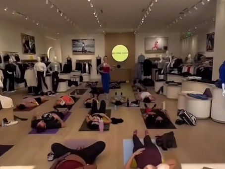 A room full of people doing yoga with a teacher standing up in the center of the room.