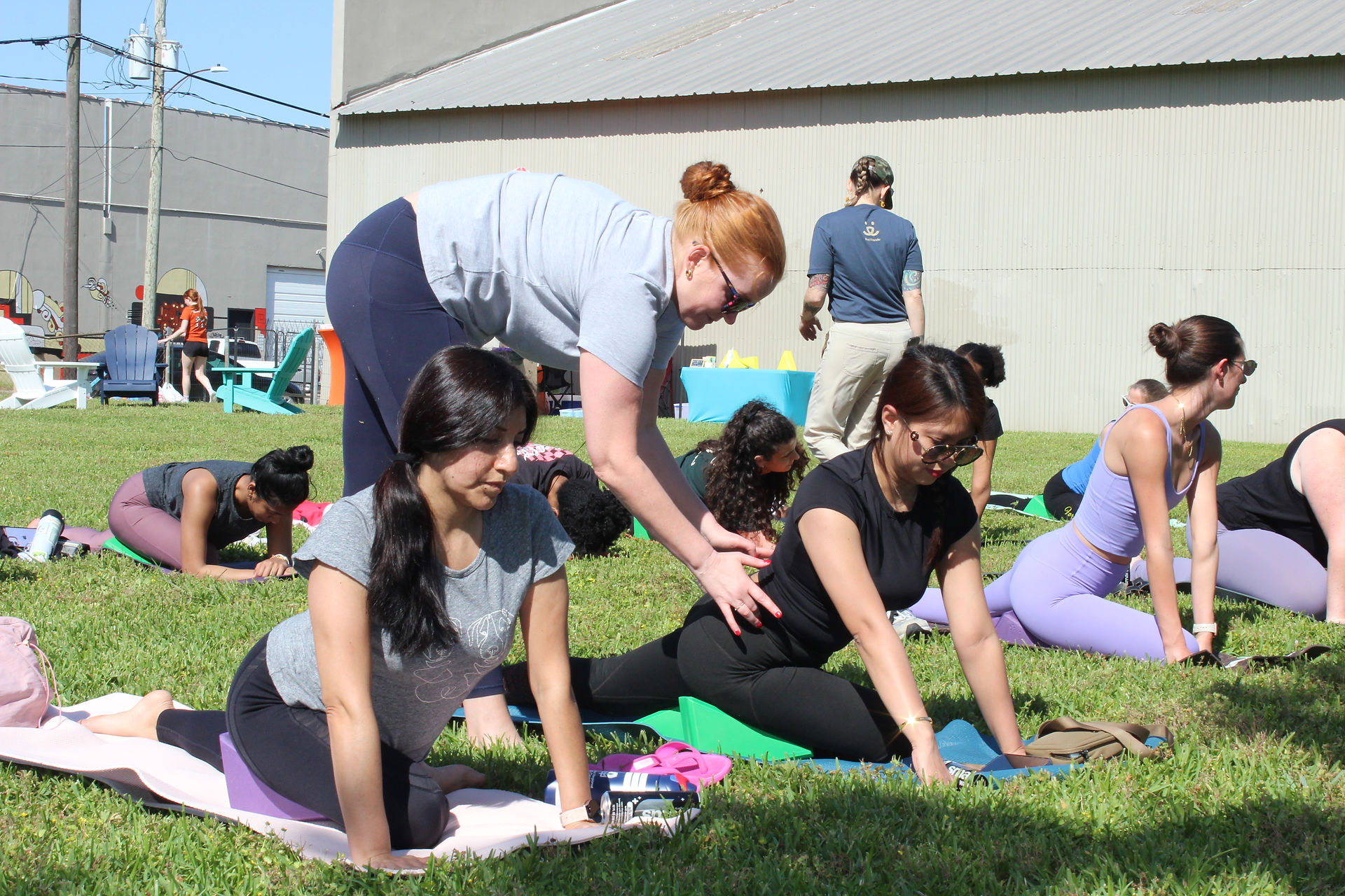 Students enjoying yoga with a teacher helping them on their mats.