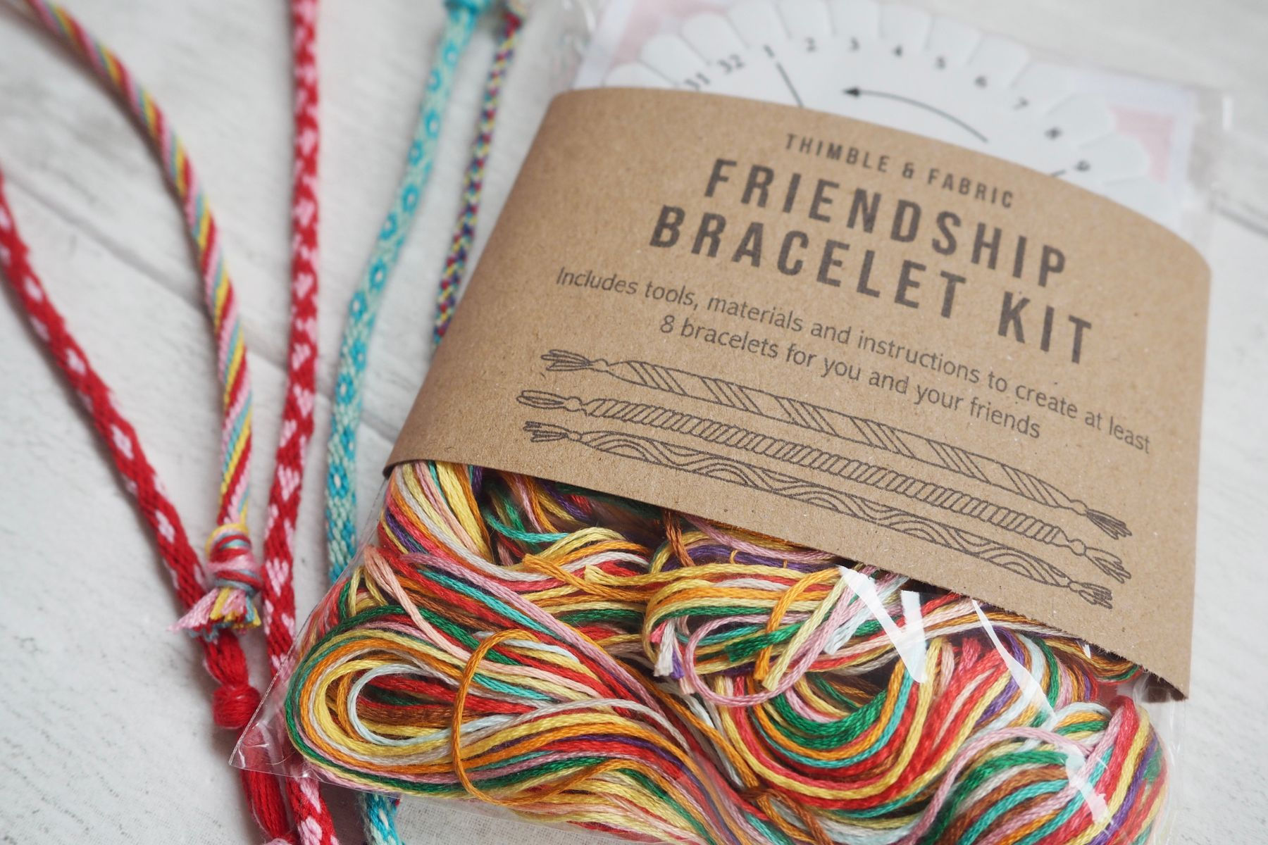 Finished rainbow friendship bracelet shown next to ecofriendly packaged kit