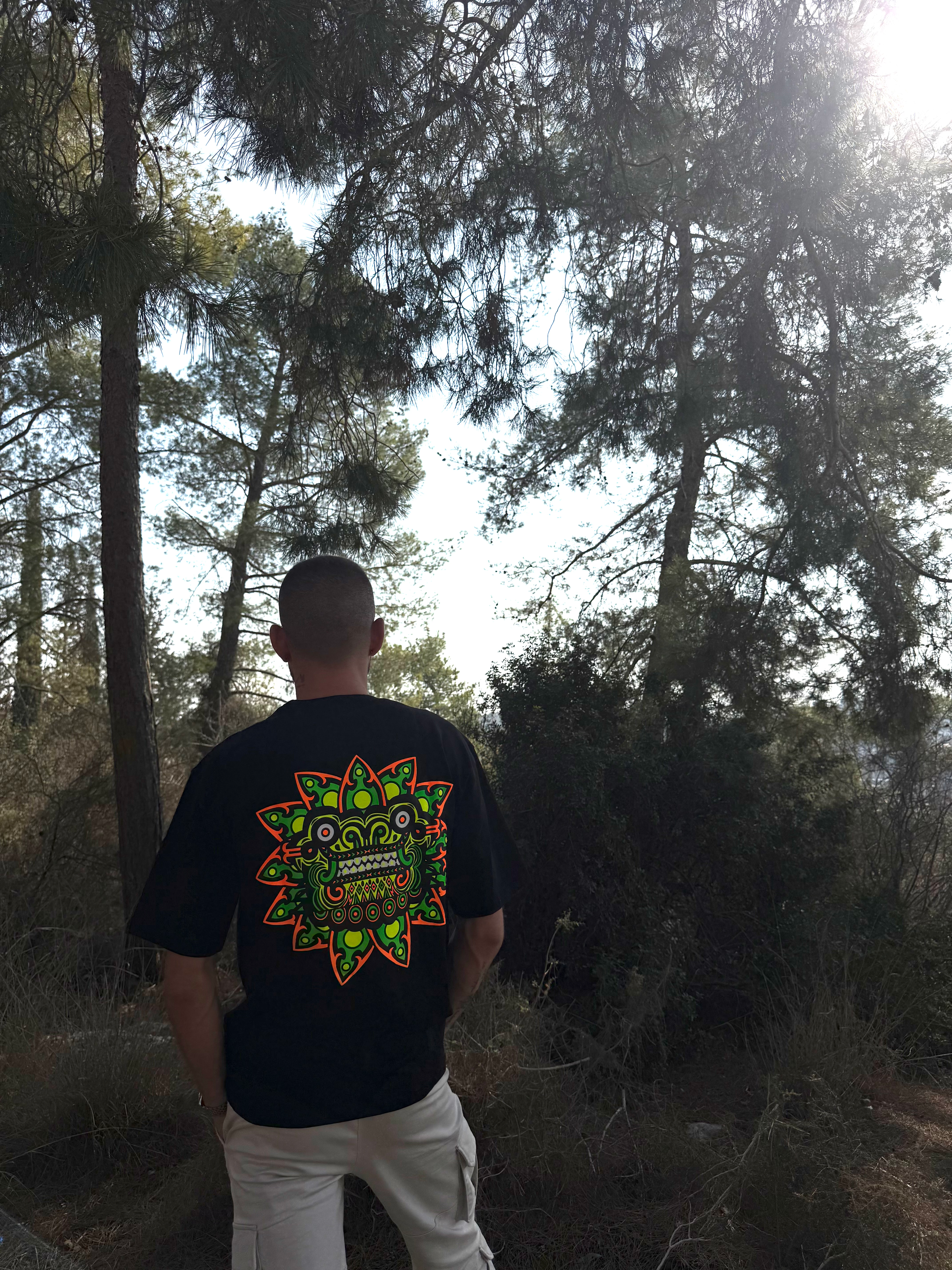 גבר עומד בגבו מול נוף יער, לובש חולצה עם הדפס. תיק צד אלכסון מבד- צבע ירוק | מיין באזר 10