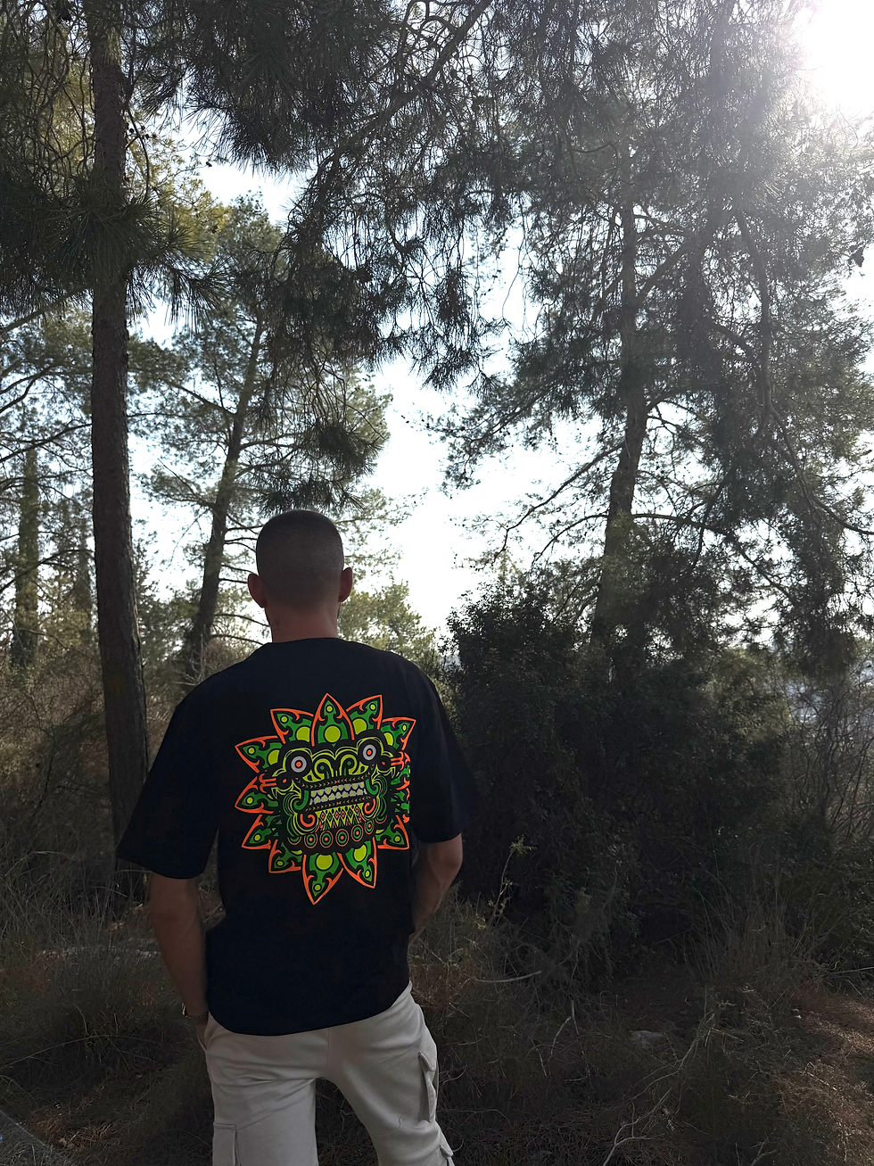 גבר עומד בגבו מול נוף יער, לובש חולצה עם הדפס. תיק צד אלכסון מבד- צבע ירוק | מיין באזר 10