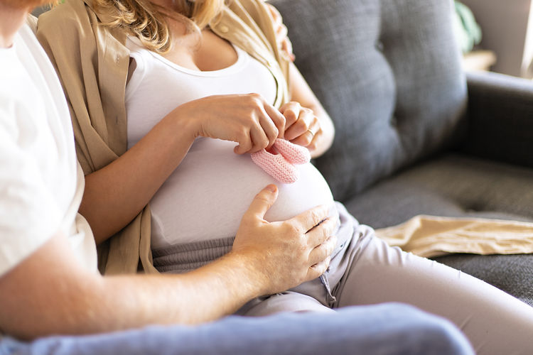 Frau ist schwanger, hält Söckchen vor ihren Bauch. Vater hat seine Hand auf den Bauch gelegt.
