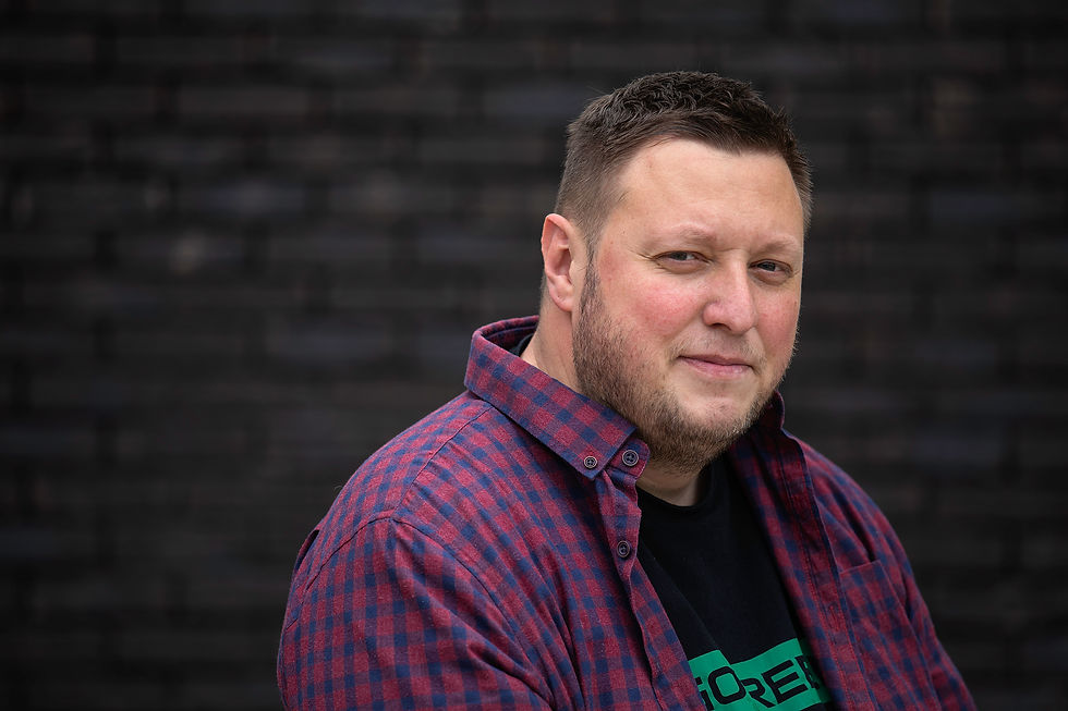 Ismir Delija, a man in his late thirties in a red and blue checkered shirt, in front of a dark background.