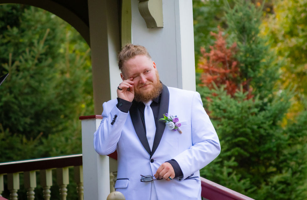 Emotional groom wipes away tears during touching outdoor wedding ceremony moment on gazebo with fall colors