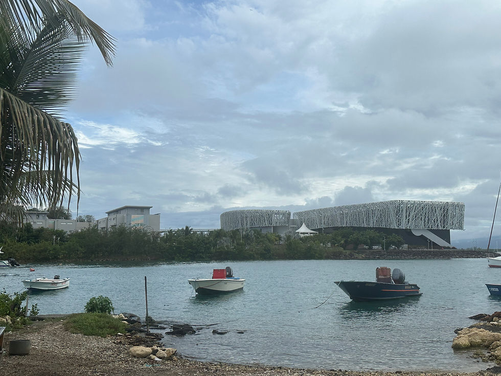 Vue sur le Mémorial ACTe entouré de verdure, de la mer et de bateaux de pêcheurs