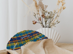 Éventail artisanal en tissu madras coloré de Guadeloupe posé sur une table avec décoration florale