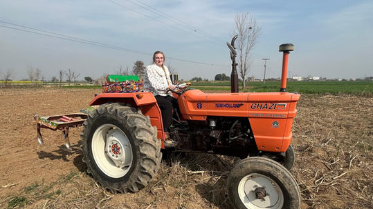 Female American student sitting on an orange painted tractor.