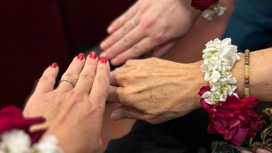 Three hands joined together with flowers around the wrists.