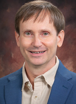 Headshot of Paul Edleman wearing a blue blazer and tan shirt.
