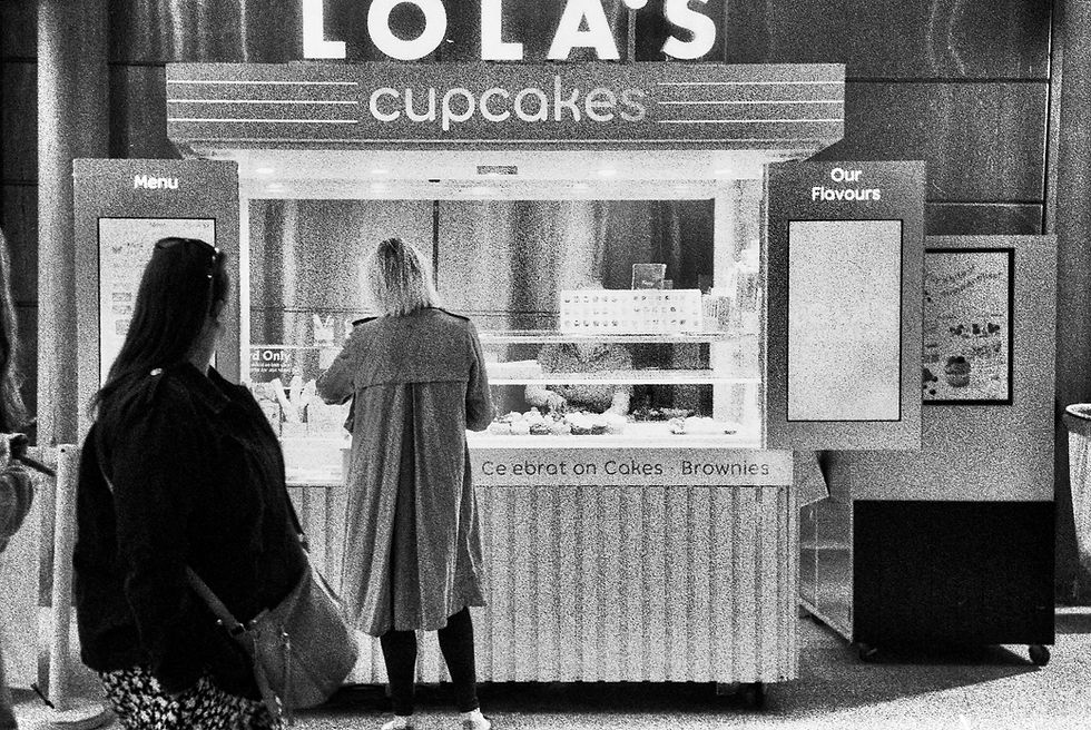 Black and white photograph of a Lola's Cupcakes stand at North Greenwich Tube Station