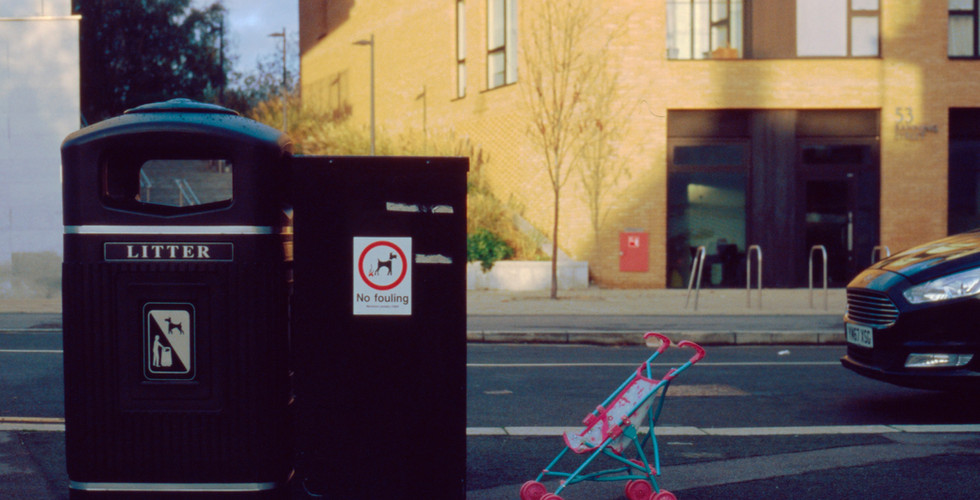 A child's dolly pram, parked next to a rubbish bin.