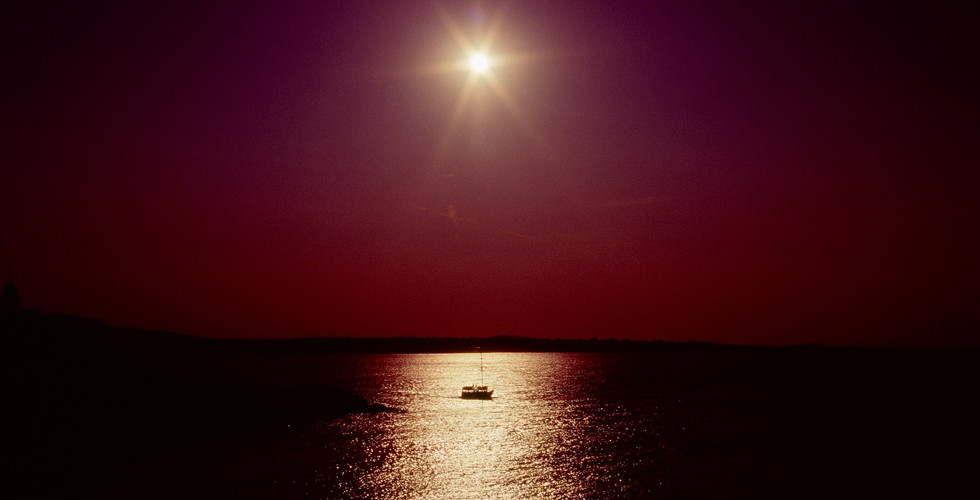 Shot directly into the sun with a reflected sun path and a boat in the centre of the reflection.