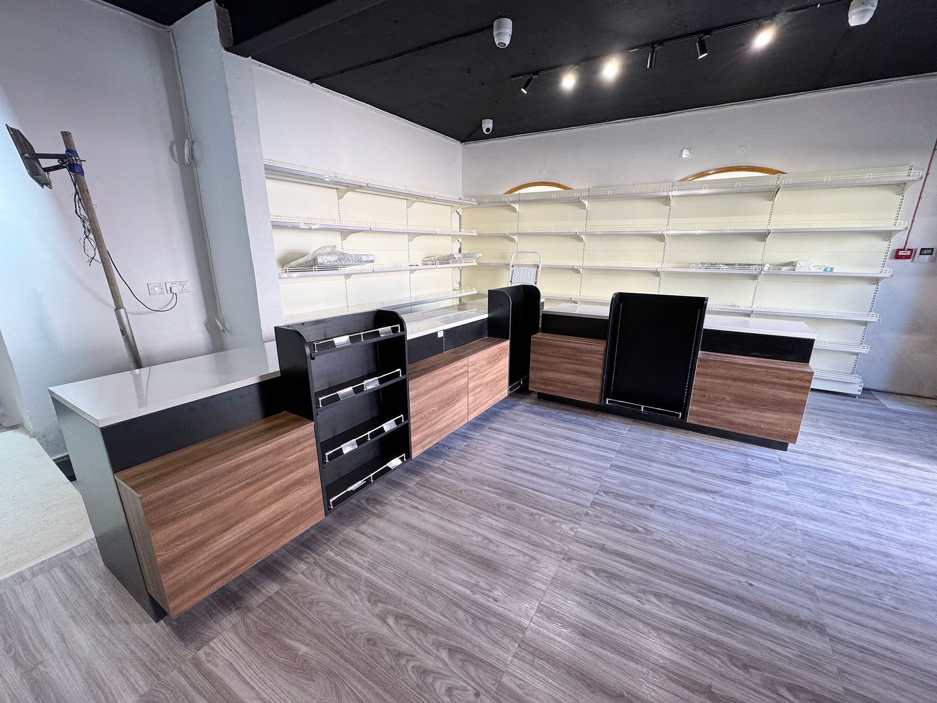 A minimalist retail checkout area with black and wood cabinetry, featuring empty shelves.