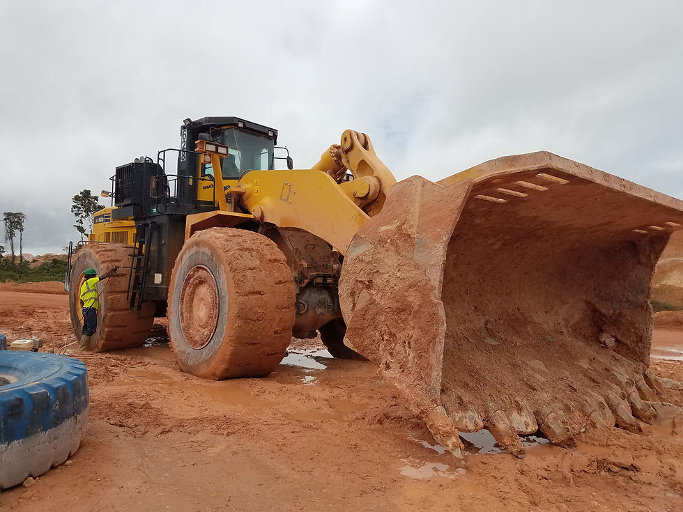 Yellow bulldozer with large muddy bucket on a construction site. Worker in yellow vest stands beside it. Overcast sky, earthy tones.
