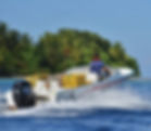 Man steering a motorboat with yellow crates in a tropical sea setting, heading towards an island with lush greenery under a clear blue sky.