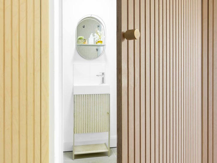 Bespoke fluted birch plywood door leading to a compact bathroom with wall-mounted basin and corrugated-front vanity unit.