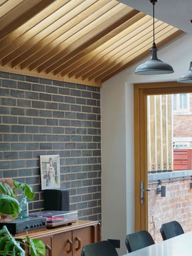 A detailed interior shot of the bespoke timber detailing below a rooflight, and exposed brick wall, in a quirky and modern home extension in Sale, designed by Manchester architects, Mulholland Architecture