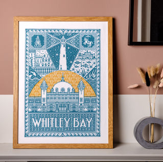 blue and yellow cross stitch sampler of whitley bay in a wooden frame on a white shelf