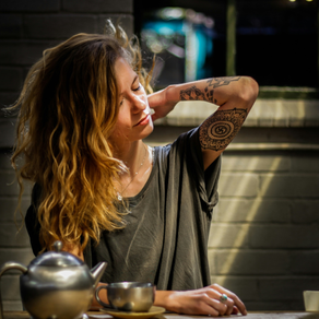 woman with tattoos making tea and looking stressed.