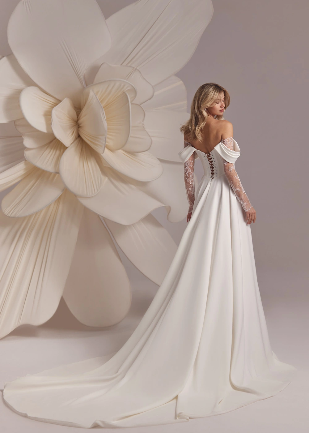 Bride wearing Baccara by Eva Lendel wedding dress, strapless neckline, with long lace sleeves and lace insert split detail 