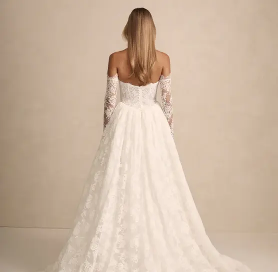 Prim lace wedding dress by Made With Love with flattering Basque waist, optional straps, structured bodice, and gathered flowing skirt — perfect for modern brides.