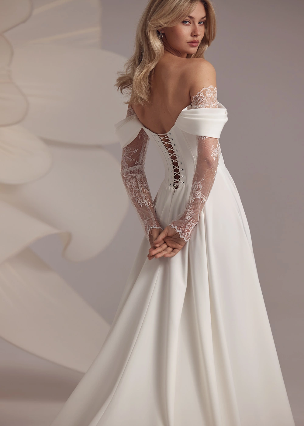Bride wearing Baccara by Eva Lendel wedding dress, strapless neckline, with long lace sleeves and lace insert split detail 
