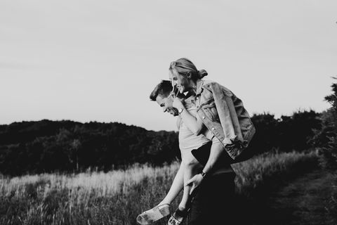 black and white image of a couple piggy backing in the woods