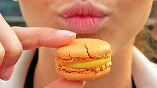 gros plan d'un beau macaron et d'une bouche pulpeuse, macaron tenu avec deux doigt prêt à être mis en bouche