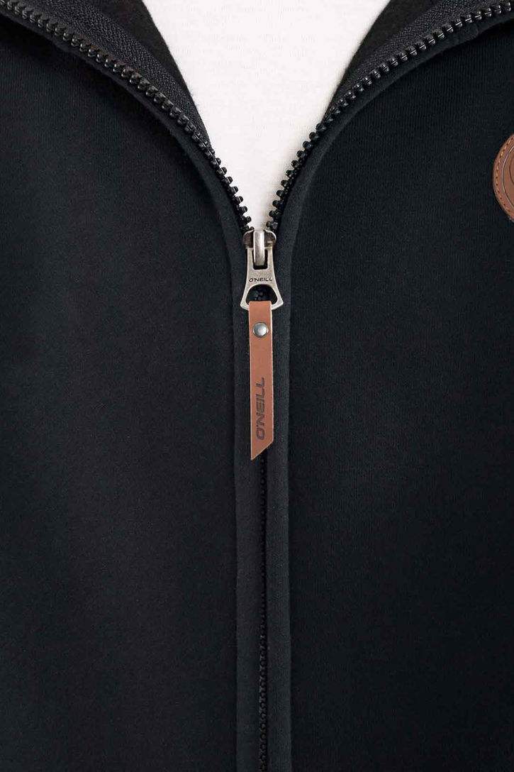 Primer plano de cierre de campera de metal con logo grabado de marca; fotografía de detalle técnico de branding.