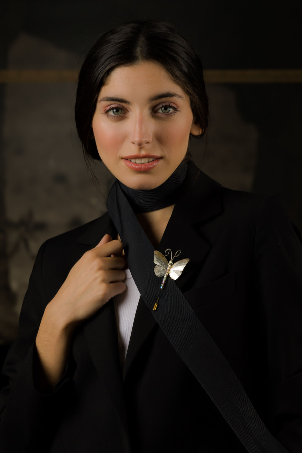 Primer plano de modelo femenina con blazer negro y broche de plata en forma de mariposa.