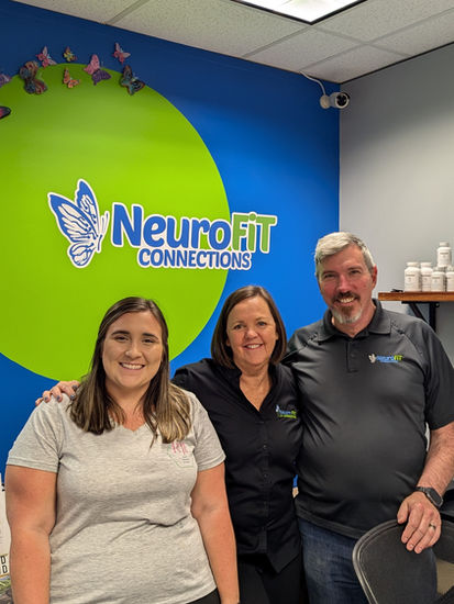 Three smiling people standing in front of the NeuroFit Connections logo on blue wall.