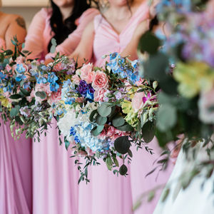 Bridesmaids holding pastel bouquets, wearing pink dresses; wedding day celebration.