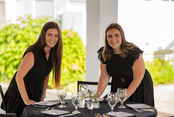 Two women of the team setting a table smiling, preparing for an event