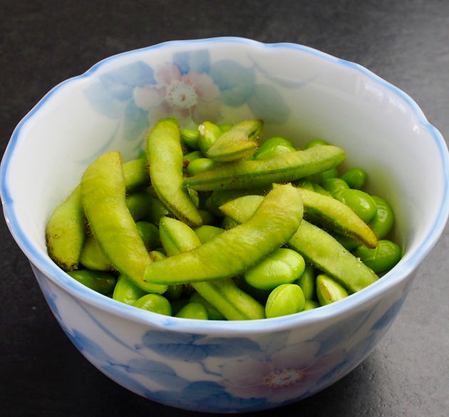 Edamame in a floral white bowl on a dark surface. Bright green pods and beans create a fresh, natural look.