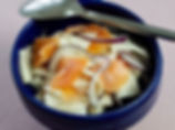 Blue bowl of salmon salad with sliced red onion and sliced turnip, topped with a spoon on a pink surface