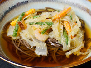 Bowl of soba noodles topped with colorful vegetable tempura in a light broth. Earthy tones with a rustic, appetizing feel.