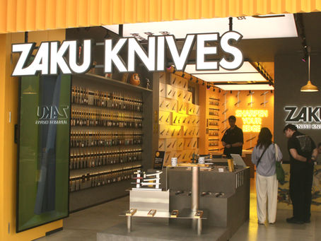 ZAKU KNIVES store interior with wall displays of knives, customers browsing, and neon sign reading SHARPEN YOUR EDGE.