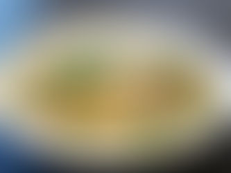 A plate of Miso Tuna spaghetti topped with shredded cheese and chopped herbs on a dark table. The dish looks fresh and appetizing.