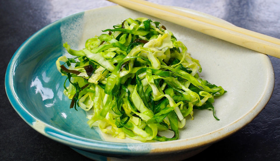 A dish of shredded cabbage with kelp in a green-blue bowl on a dark surface, accompanied by wooden chopsticks.