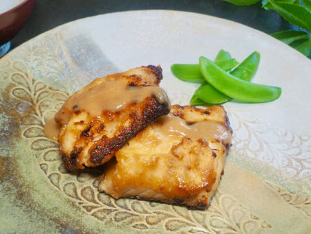 Two miso glazed grilled cod fillets on a patterned plate with snap peas, close-up tabletop food presentation