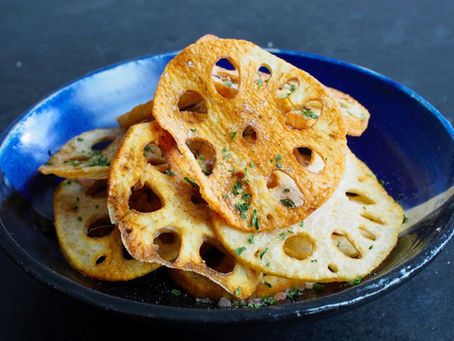 Crispy fried lotus root slices with herbs piled in a blue bowl on a dark background.