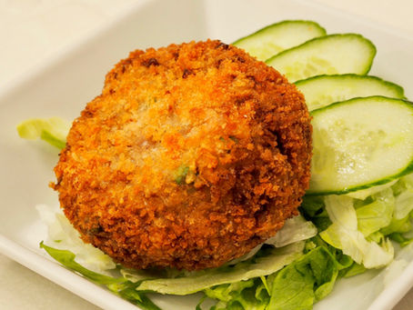 Golden Menchi Katsu on a bed of lettuce with sliced cucumbers, served on a white plate. The setting is simple and appetizing.