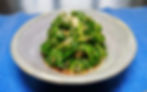 Plate of seasoned spinach topped with sesame seeds, served on a gray dish over a blue placemat. Goma Ae.